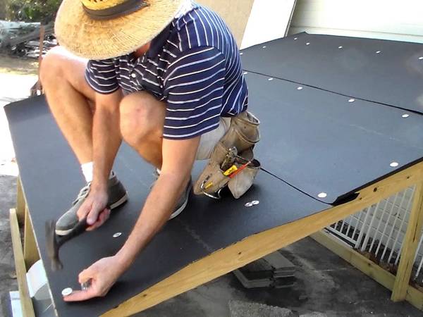 Un homme installe le feutre de toiture avec des clous.