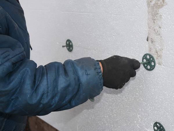 Un trabajador está instalando un tablero de aislamiento de espuma con clavos de aislamiento de plástico.